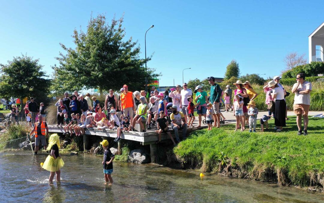 a large group of people gather at the jetty beside the duck race finish line