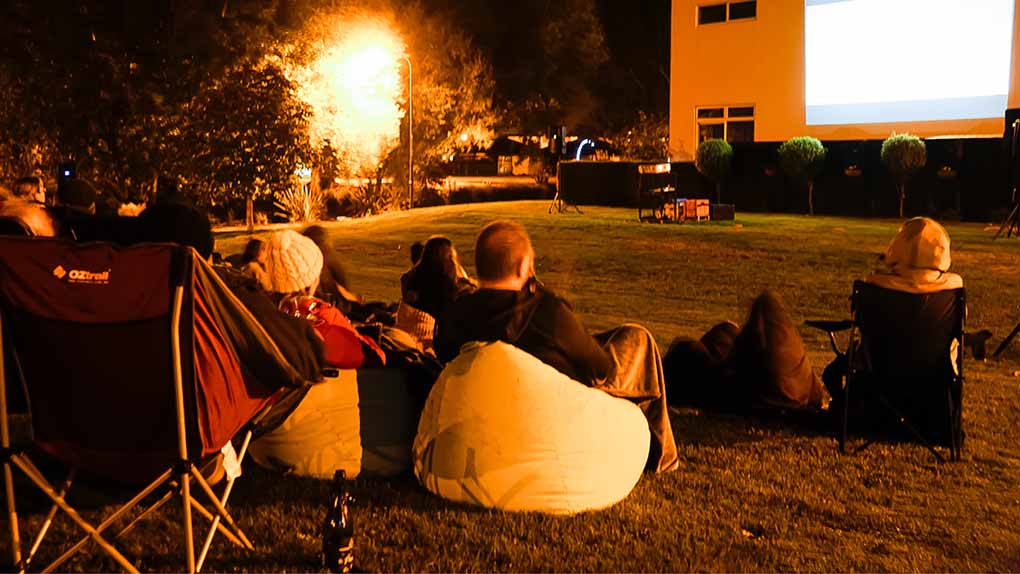 people sitting on chairs and bean bags at night watching an outdoor movie screen