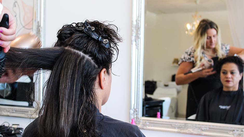 woman sitting in front of a mirror have her hair blow dried