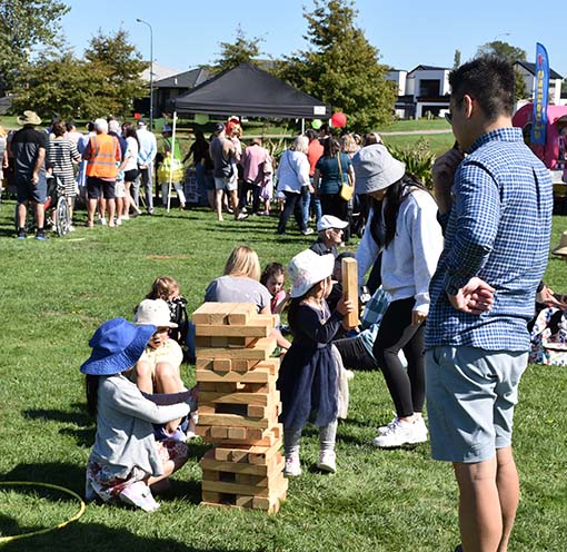young children play giant jenga on the grass at a community event